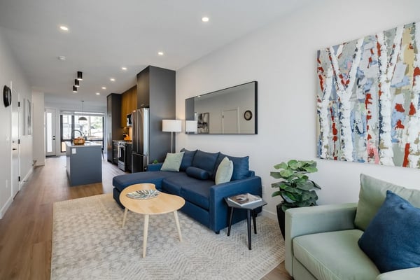 Open-plan living room with blue sofa, wood coffee table, and kitchen with dark cabinetry in background