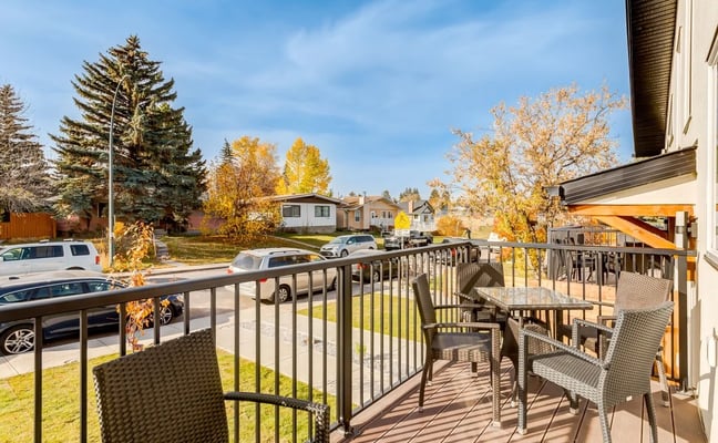 Residential deck with metal railing and patio furniture overlooking suburban street with parked cars and autumn trees